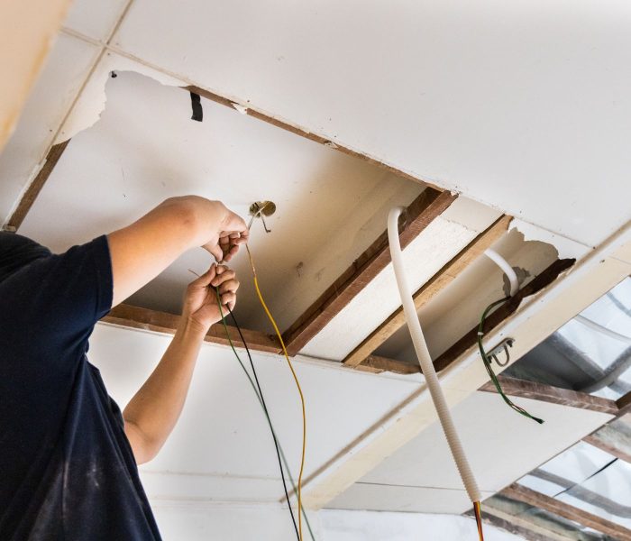 Electrician concealing electicity power wire lines within plastic tube embedded into ceiling